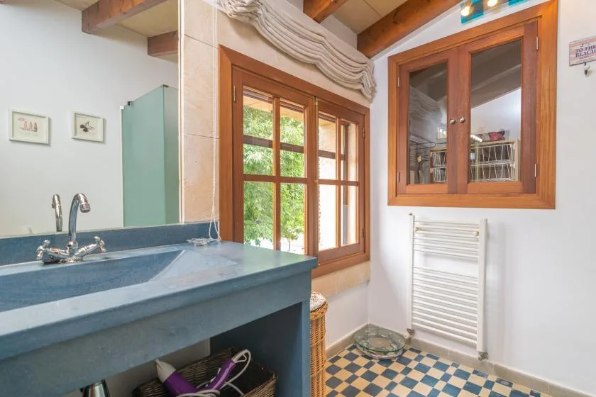 A bathroom with a blue vanity, wooden-framed windows, and patterned floor tiles.