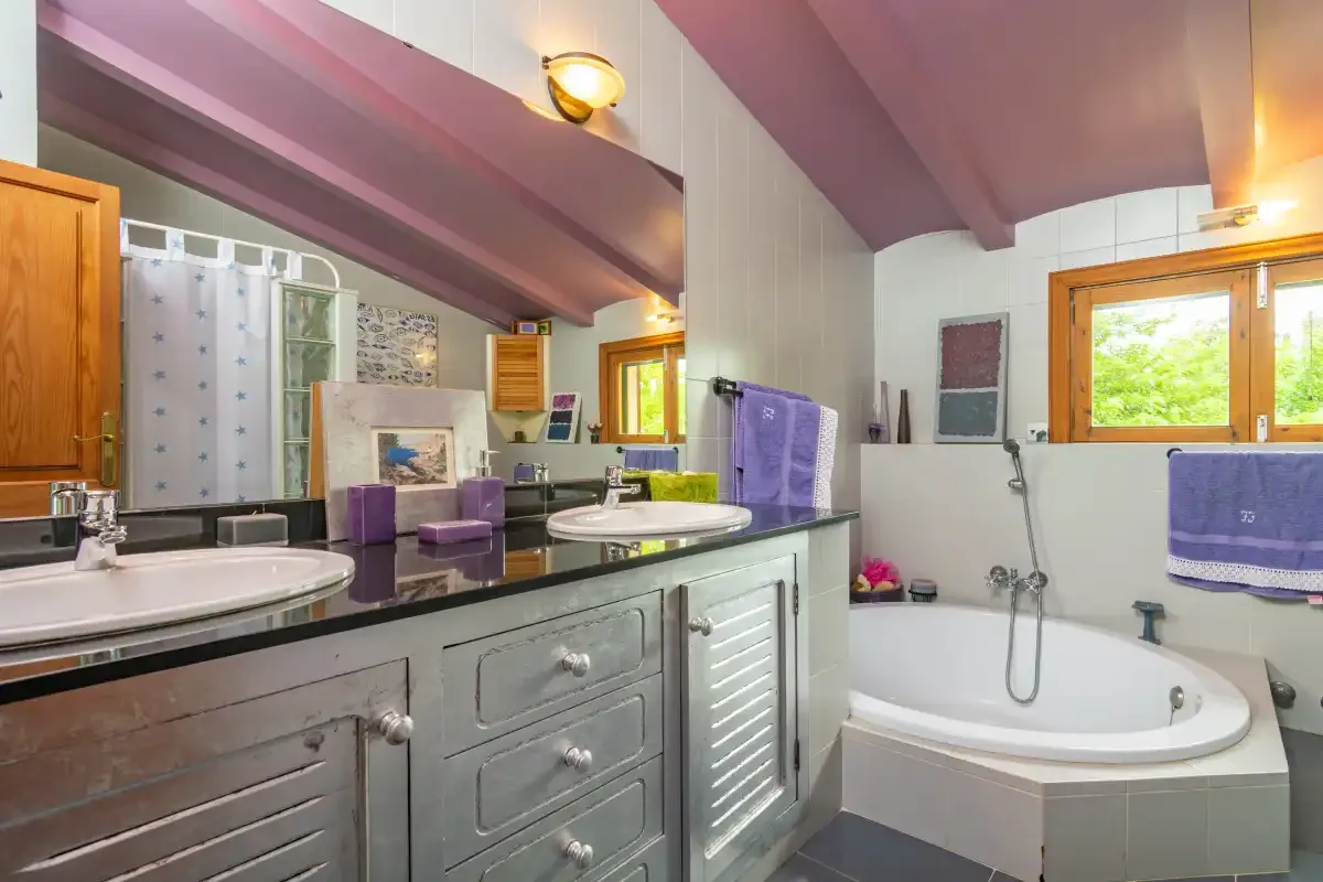 A bathroom with a wide vanity, mirrors, and a bathtub beneath a sloped ceiling.