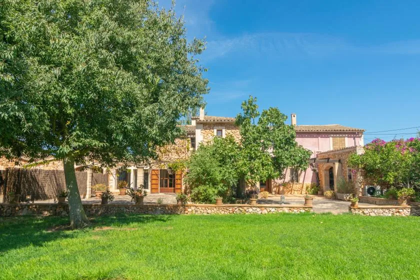A landscaped garden lawn sits in front of a stone house with trees and shrubs.