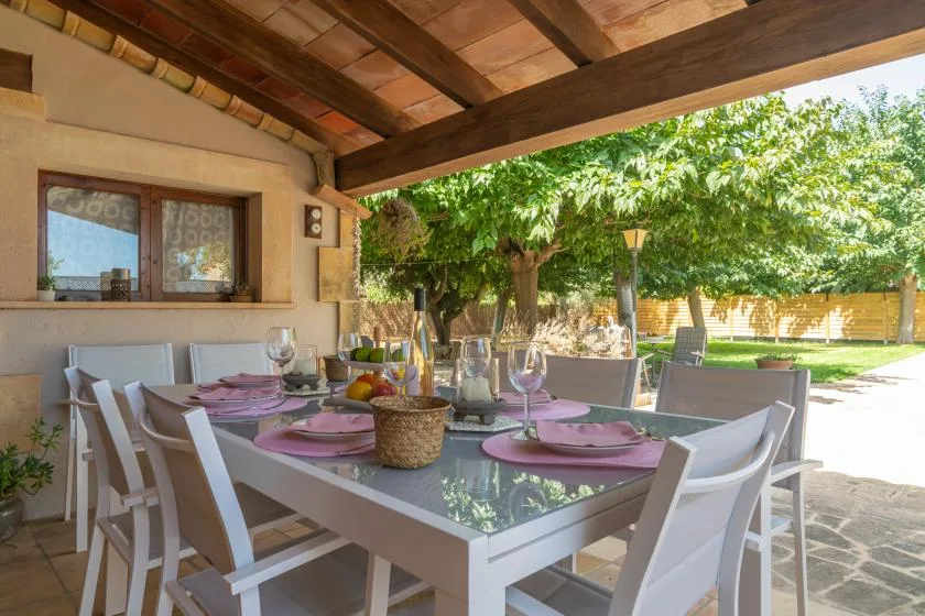 A covered outdoor dining area with a table set with pink plates.