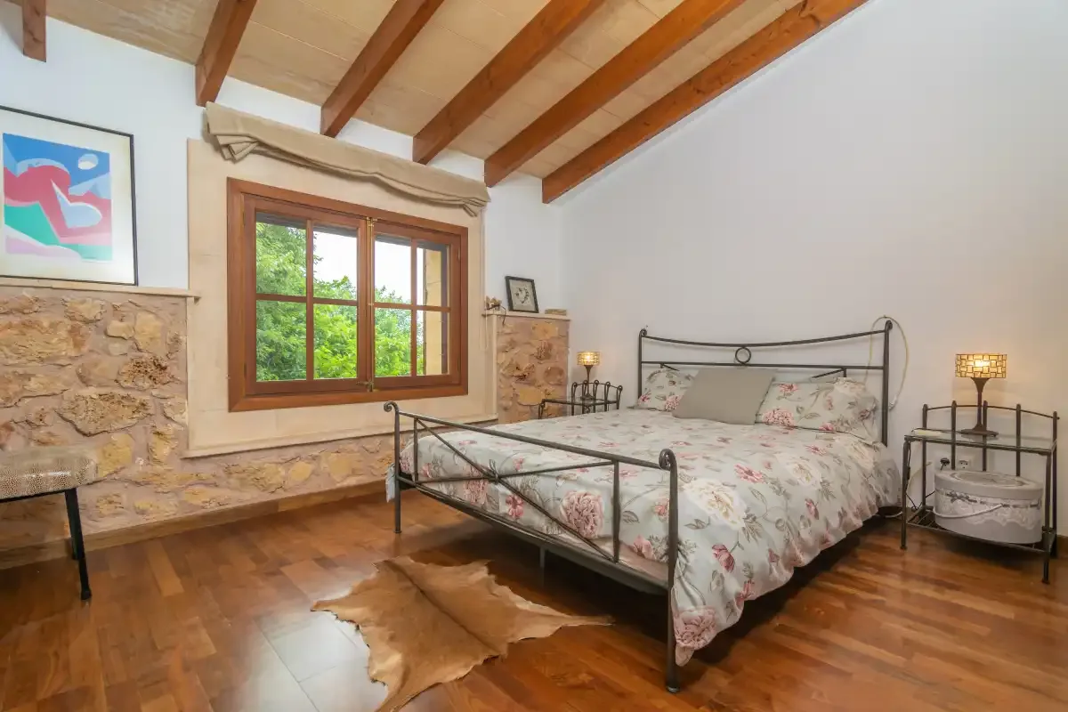 A bedroom with a metal bed, floral bedding, and exposed wooden ceiling beams.