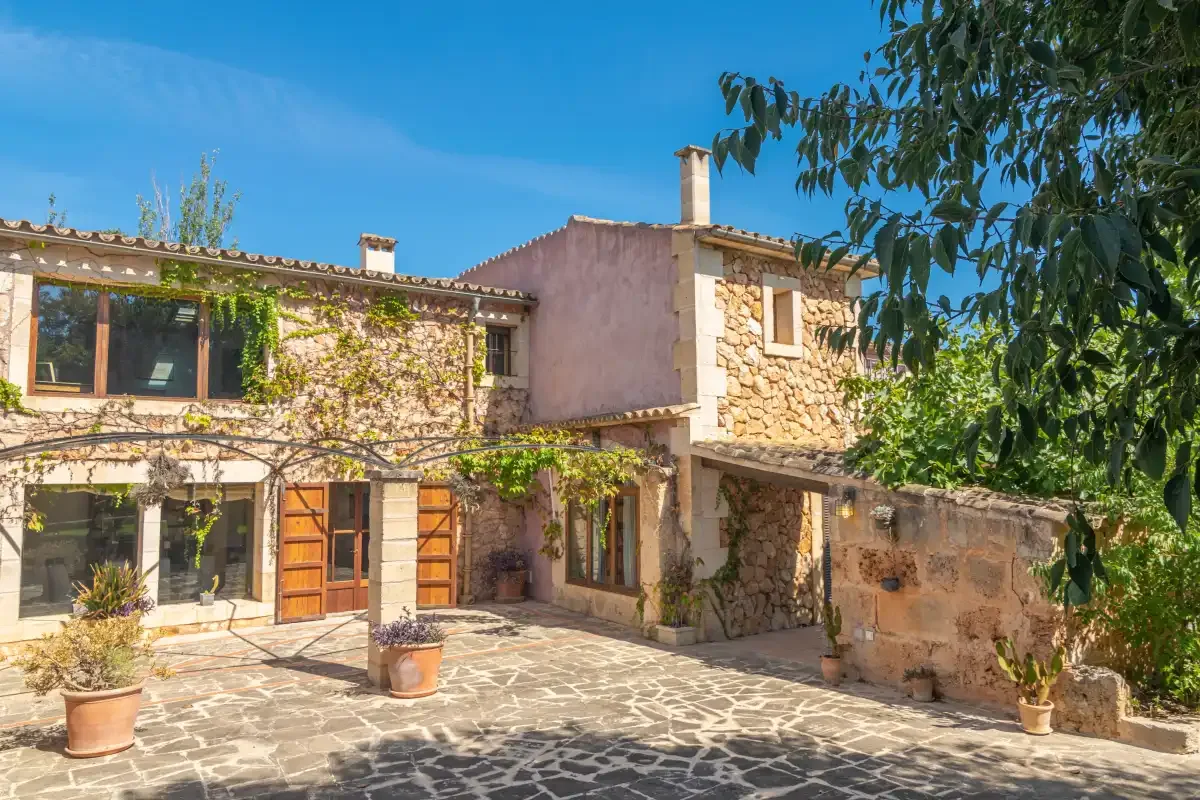A stone house with a paved courtyard and leafy vines.