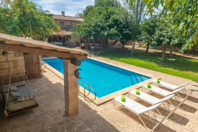 An outdoor swimming pool beside a shaded patio and lounge chairs.
