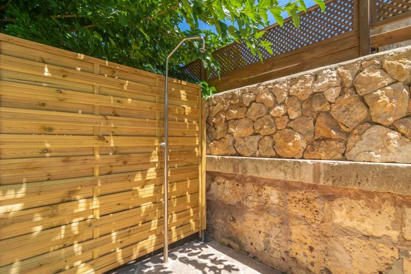 An outdoor shower stands beside wooden screening and a stone wall.