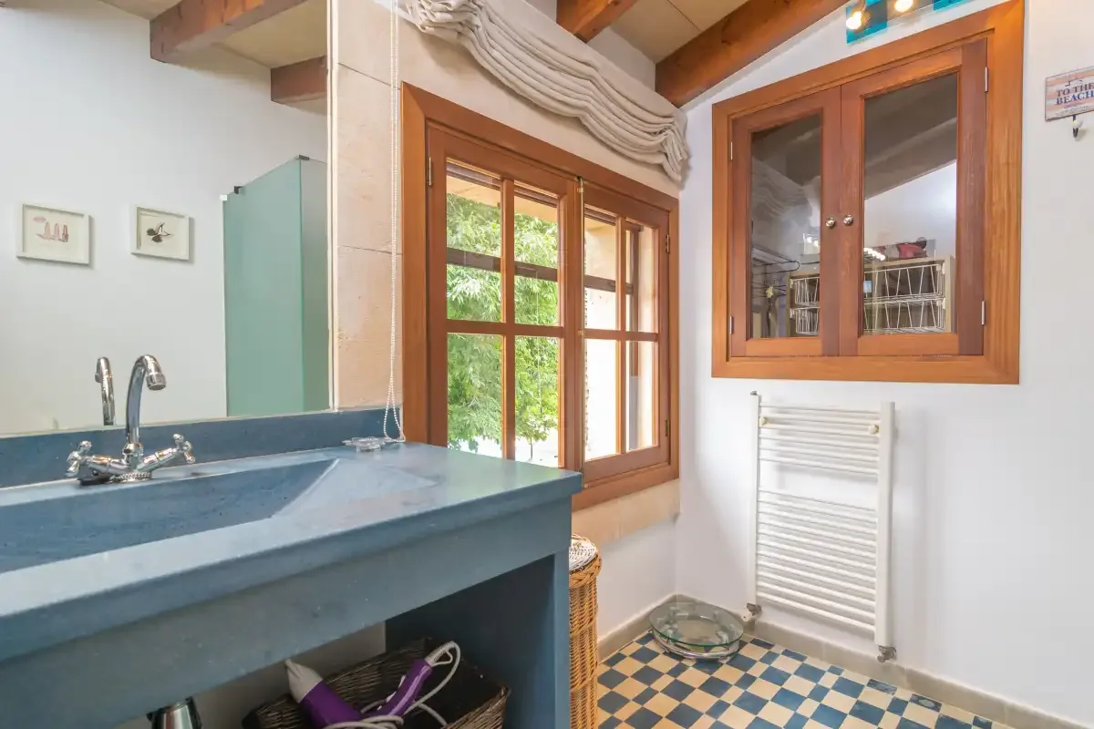 A bathroom with a blue sink, wooden-framed windows, and a tiled floor.