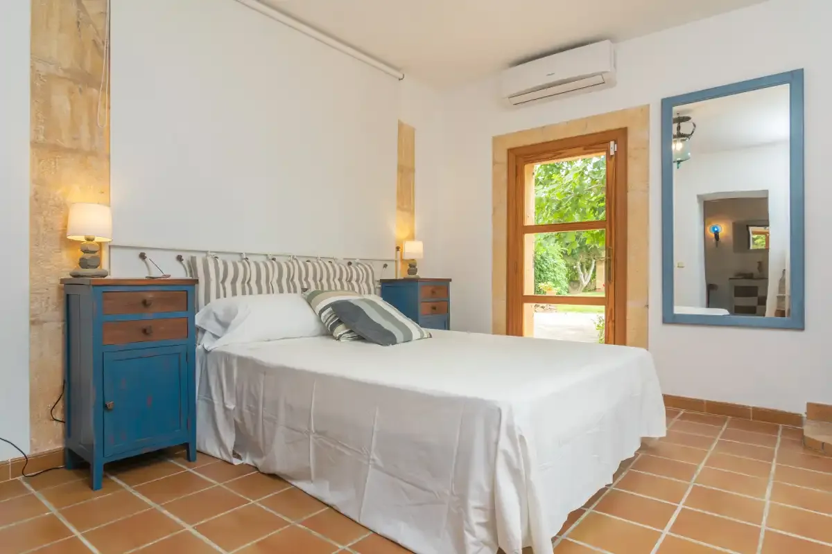 A bedroom with a neatly made bed, bedside tables, and a window.