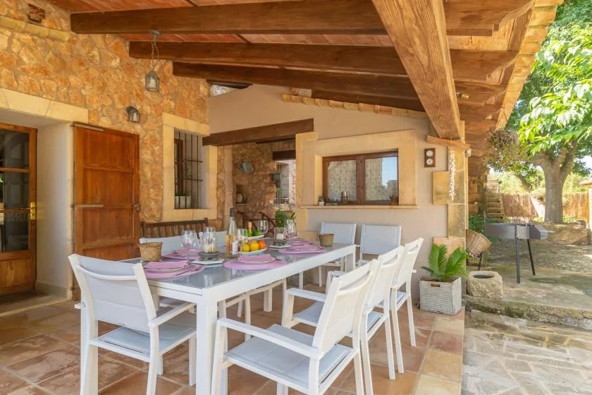 A covered outdoor dining area with a table and chairs beside a stone-and-plaster building.