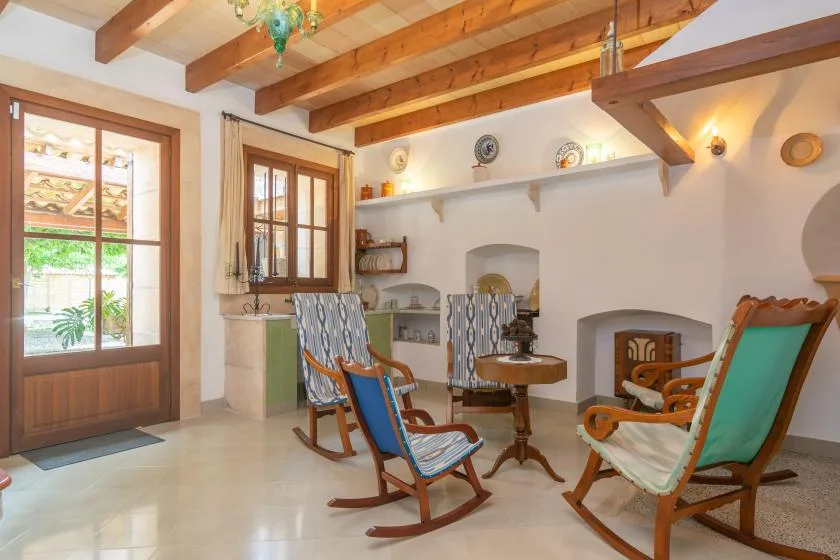 A bright sitting room with rocking chairs, wooden ceiling beams, and a small table.