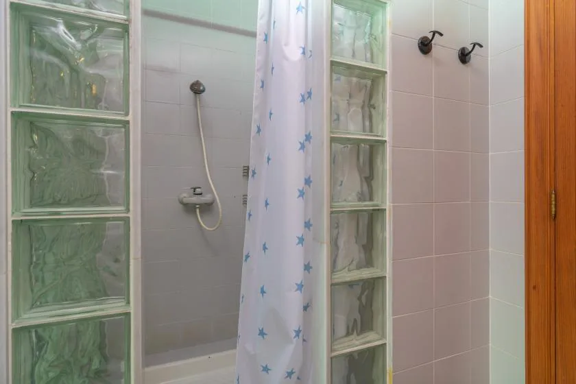 A tiled bathroom with a shower curtain and glass block panels.