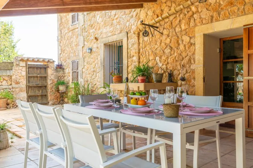 A dining table is set on a stone-walled patio beneath a wooden roof.