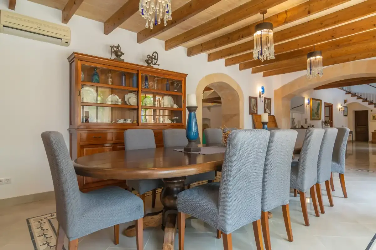 A dining room with a long table, upholstered seating, and exposed ceiling beams.
