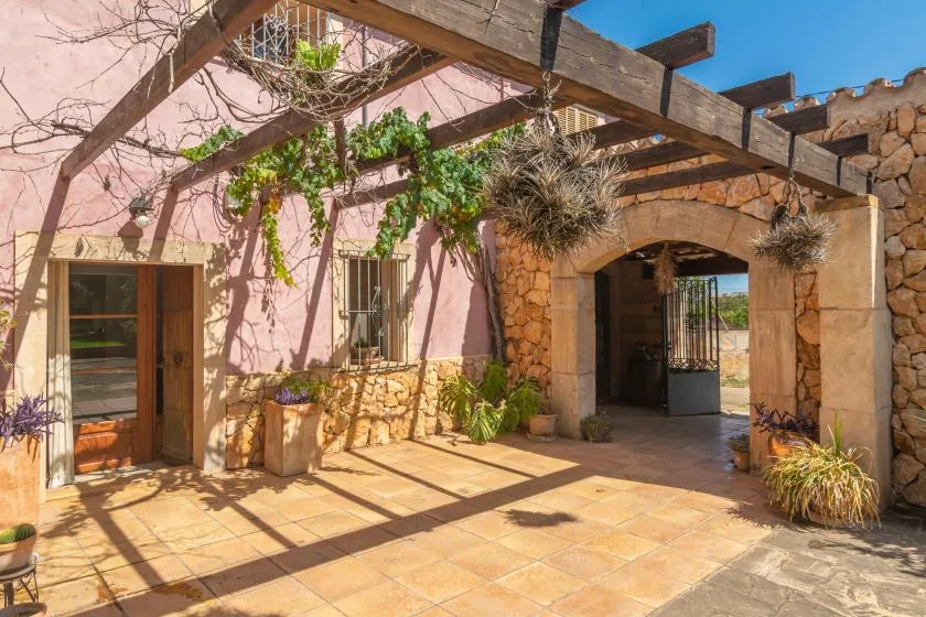 A sunlit stone courtyard has a large arched entrance and wooden beams overhead.