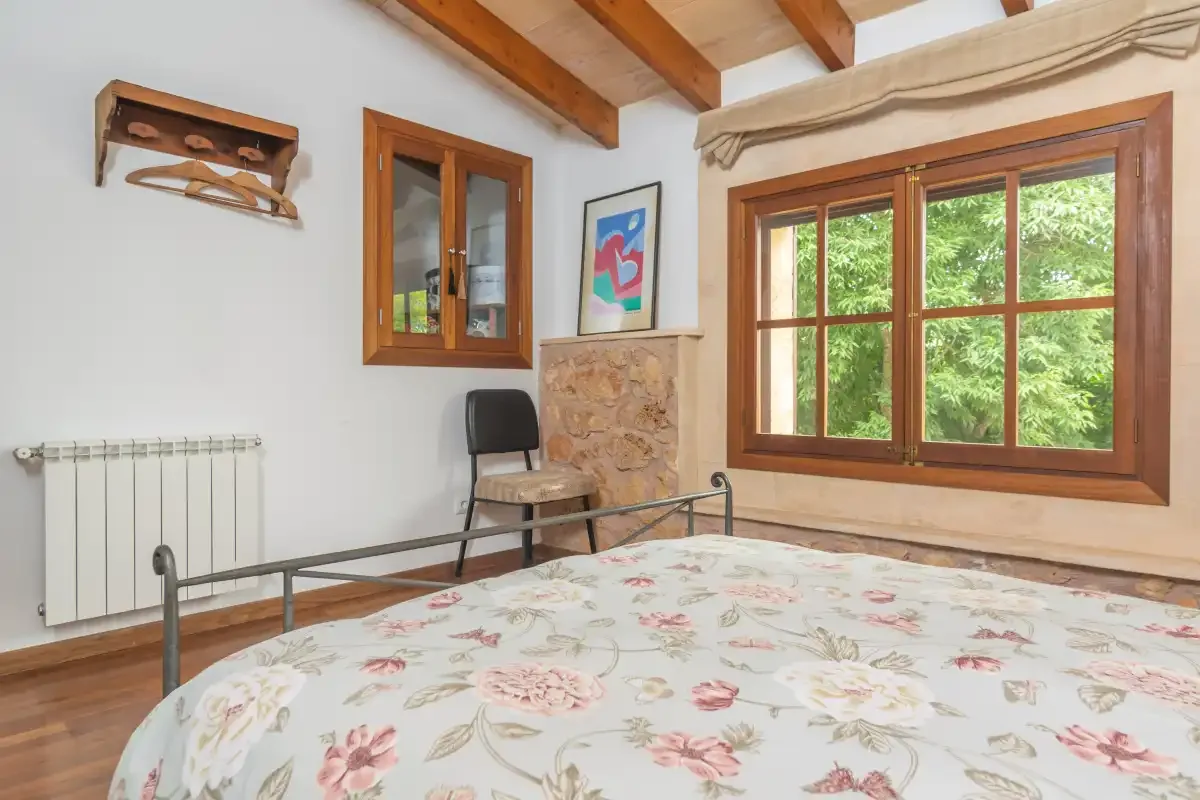 A bedroom with a floral bedspread and a large wooden-framed window.