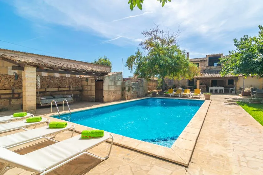 An outdoor swimming pool sits beside a stone patio and shaded seating area.