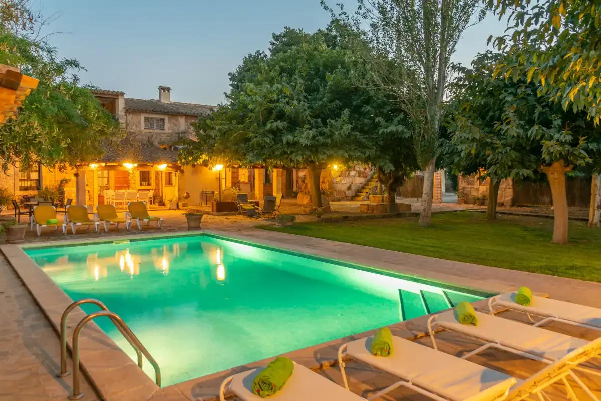 A swimming pool and lounge chairs sit in a landscaped courtyard beside a warmly lit building.
