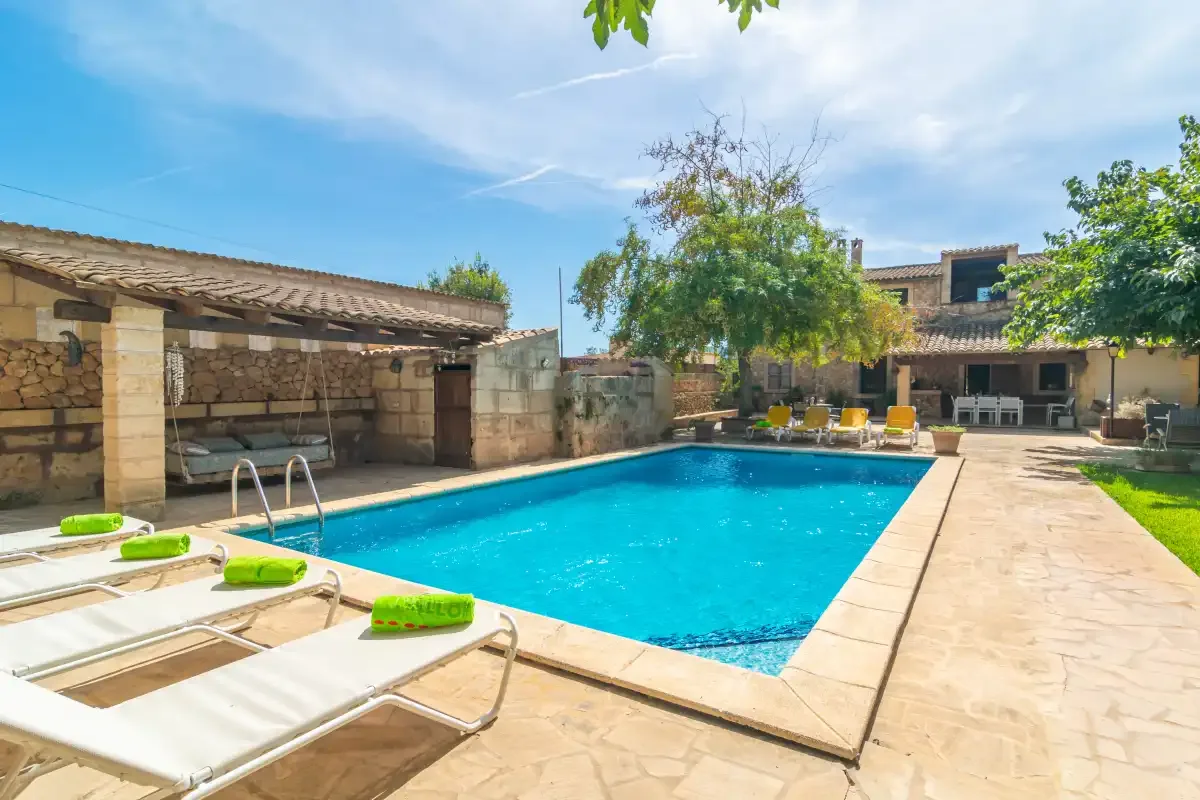 An outdoor swimming pool beside a stone patio and shaded seating area.