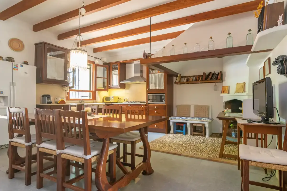 A dining area with a wooden table and chairs beside a kitchen and living area.
