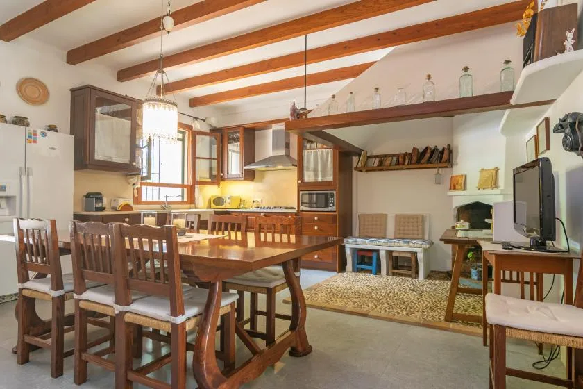 A dining area with a long wooden table and chairs beside an open kitchen.
