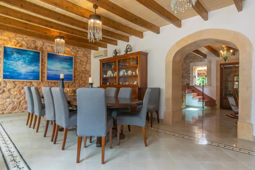 A dining room with a long table and chairs beneath exposed wooden ceiling beams.