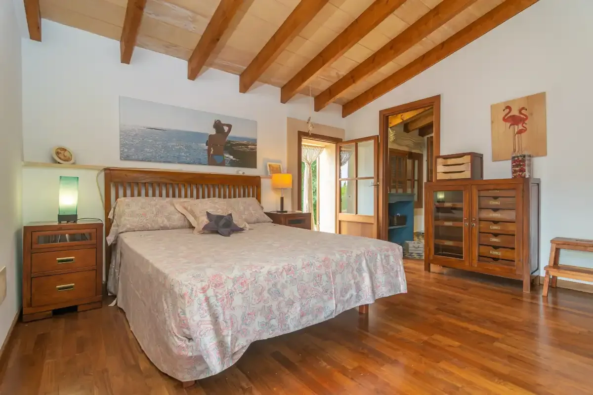 A bedroom with a large bed, wooden furnishings, and exposed ceiling beams.