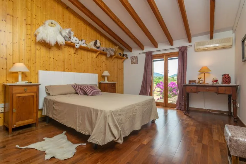 A bedroom with a large bed beneath exposed wooden ceiling beams.
