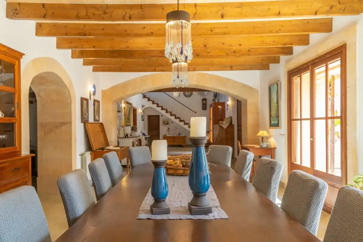 A dining room with a long table and seating beneath exposed wooden ceiling beams.