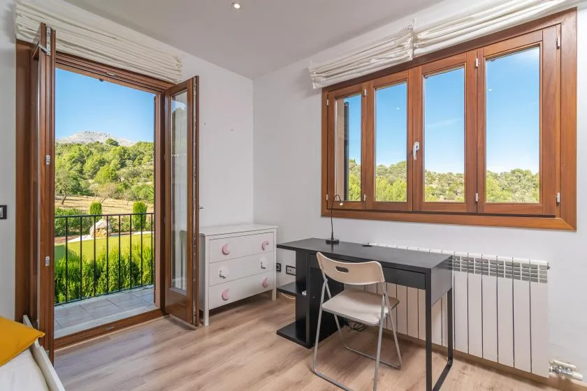 A bright room with a desk beside large windows and an open balcony door.