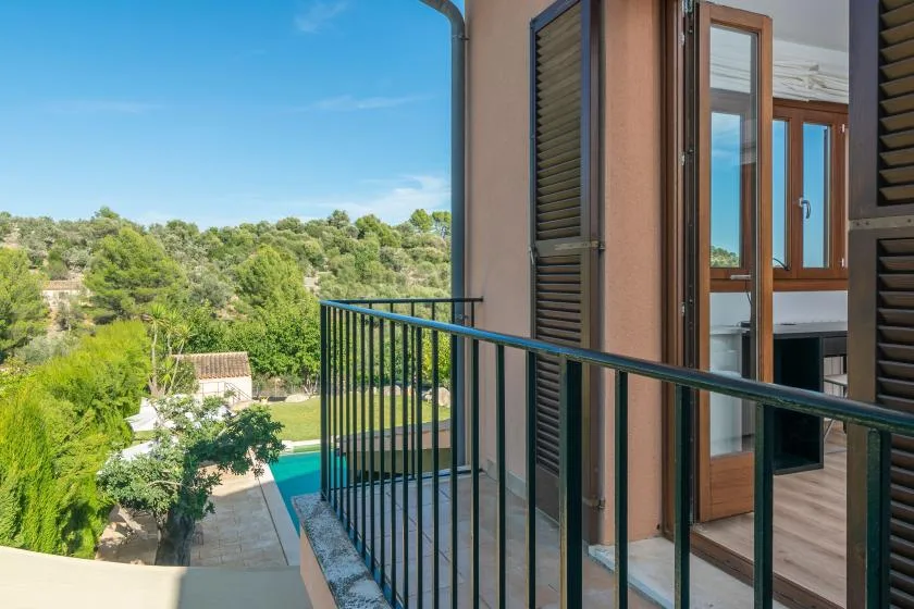 A balcony with a dark railing overlooks a green, tree-filled landscape.