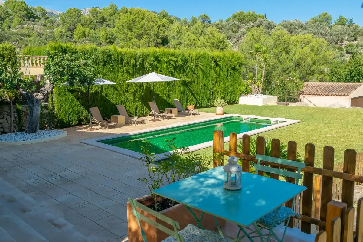 An outdoor pool and patio are surrounded by greenery and seating.