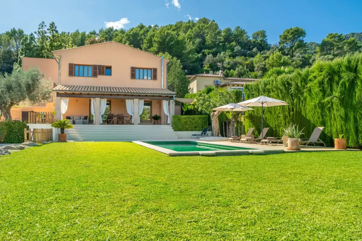 A house and swimming pool overlook a spacious lawn, with trees behind.
