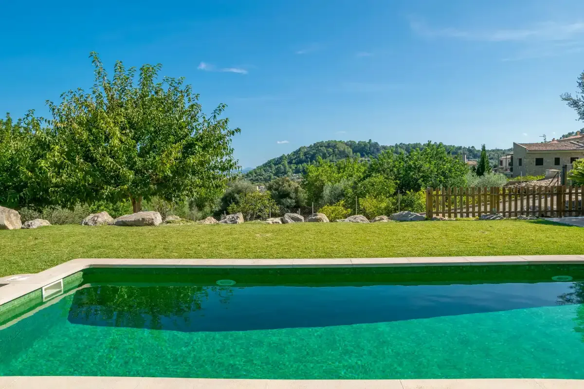 A swimming pool beside a grassy lawn, with trees and hills in the background.