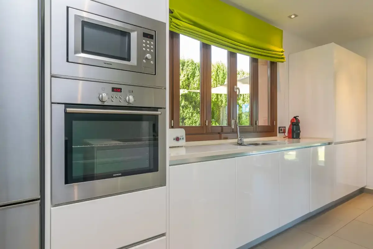 A modern kitchen with built-in appliances, white cabinets, and a window.