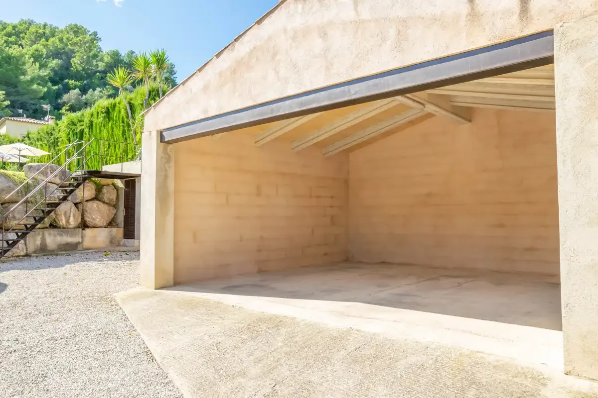 An open garage with a paved driveway and greenery nearby.