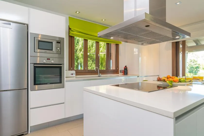 A bright modern kitchen with a large white island and a window overlooking greenery.