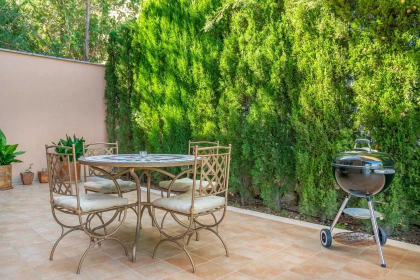 A tiled outdoor patio with a table and chairs beside a hedge.