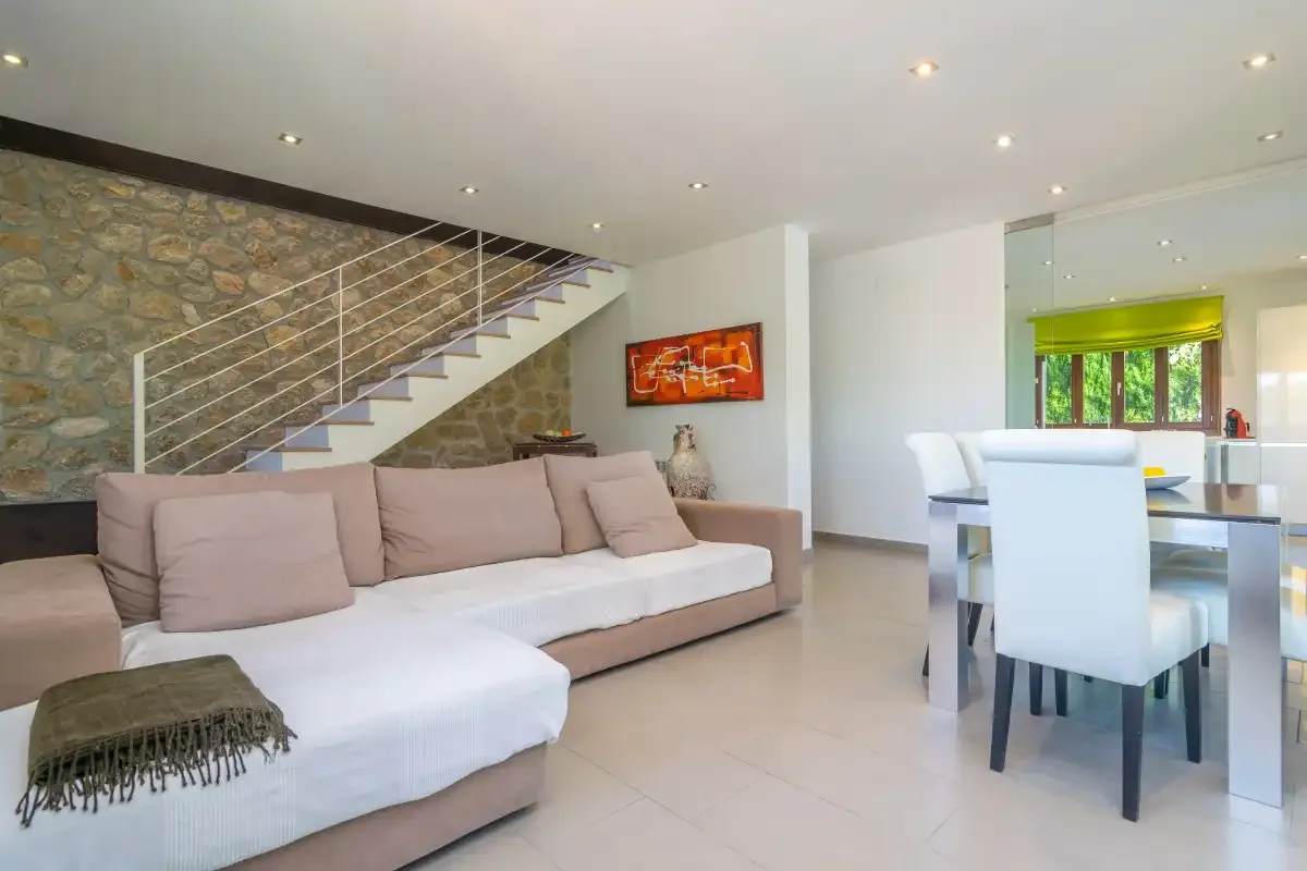 A bright open-plan living and dining area with a staircase along the stone wall.