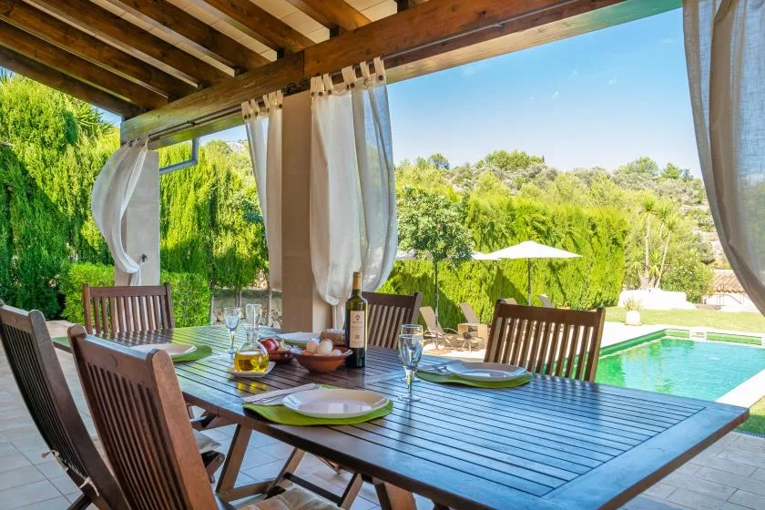 A covered patio dining area overlooks a swimming pool and green hedges.