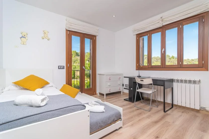 A bright bedroom with a bed, desk, and large windows.