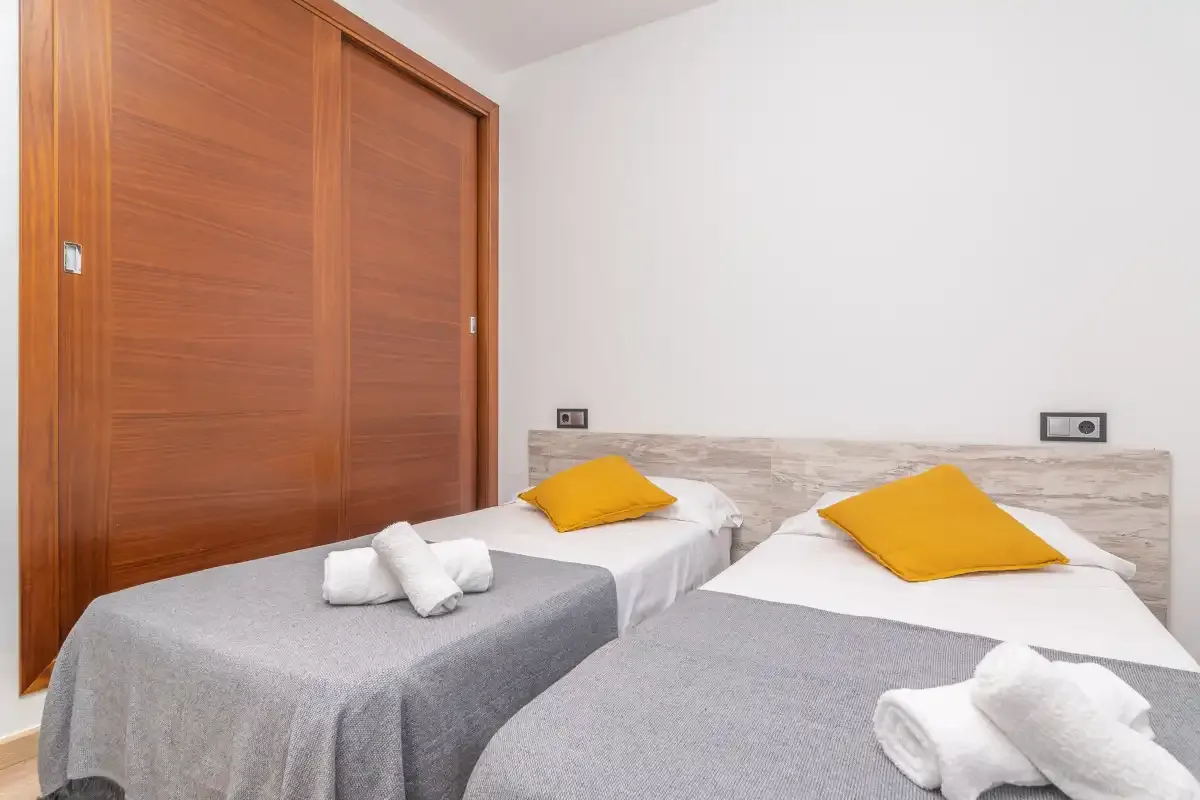 A bedroom with two beds, gray bedding, and yellow pillows.