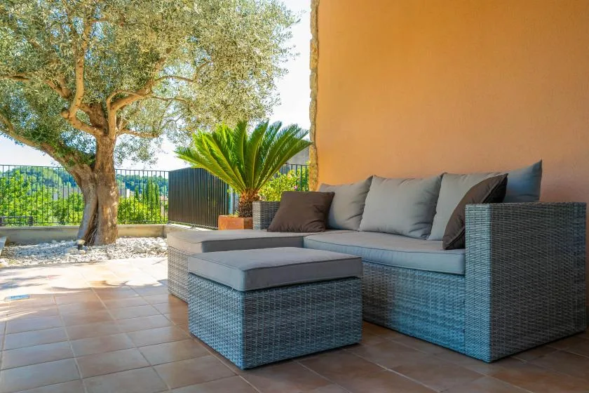 A tiled outdoor patio with cushioned seating beside a leafy tree.