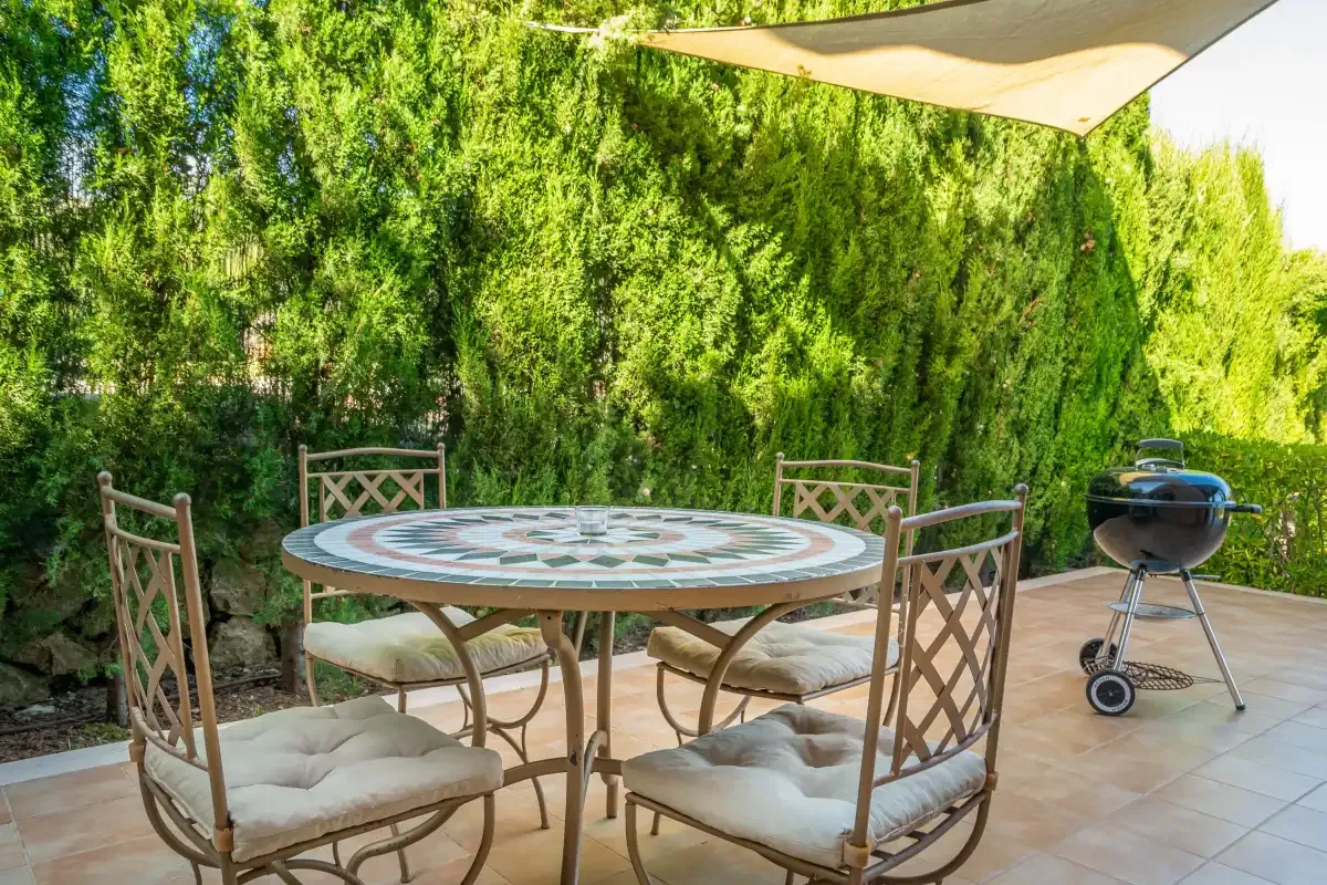 An outdoor dining area with a round table, seating, and a barbecue.