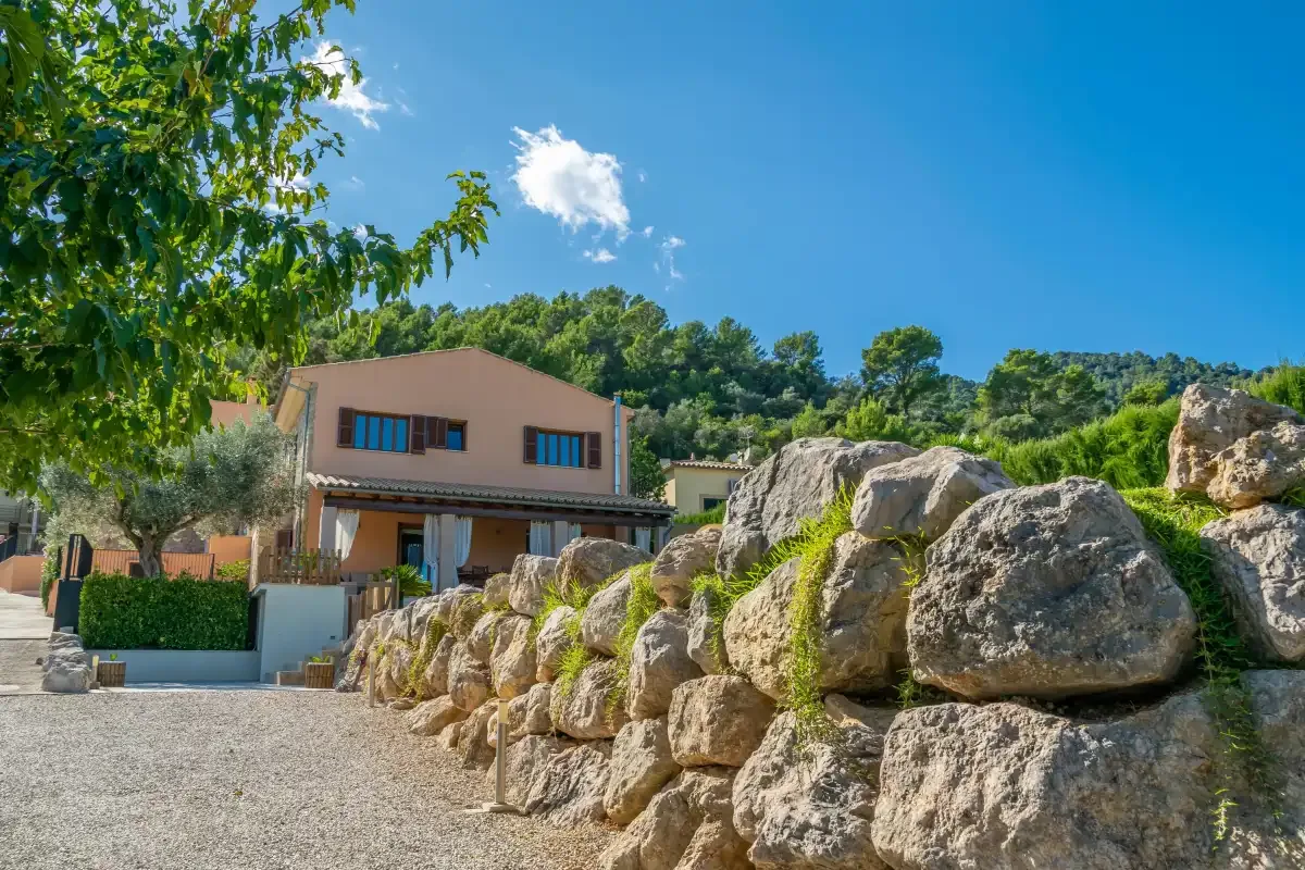 A house stands beside a gravel driveway and a line of large rocks.