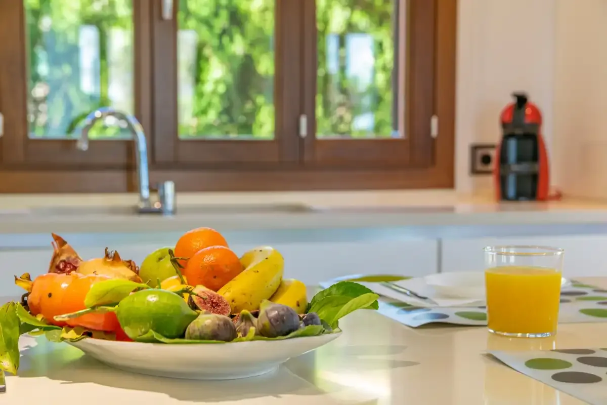 A kitchen counter holds a bowl of fruit beside a glass of juice.