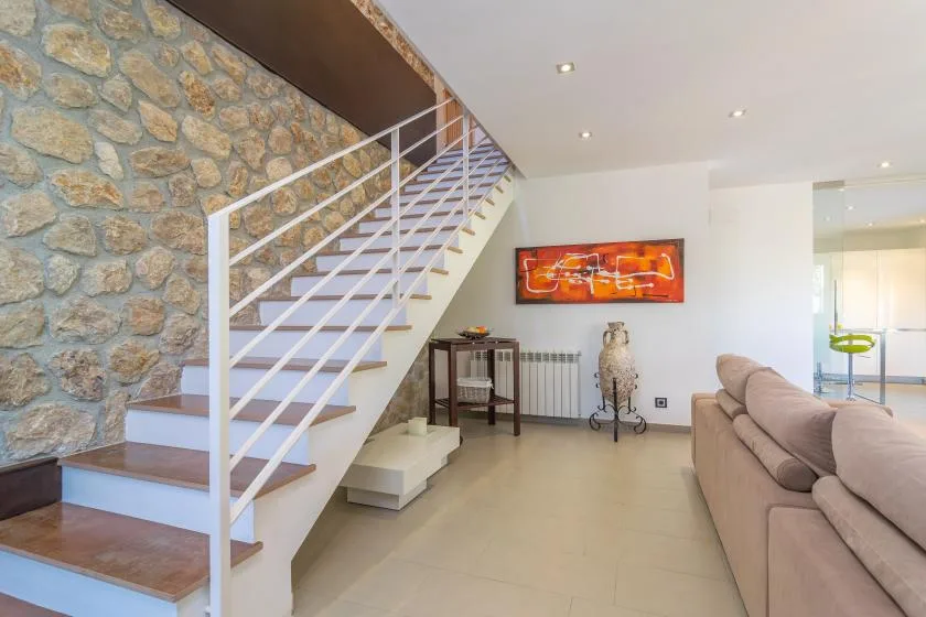 A living room with a staircase beside a stone wall and seating.