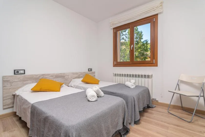 A bedroom with two beds, gray bedding, and a window overlooking trees.