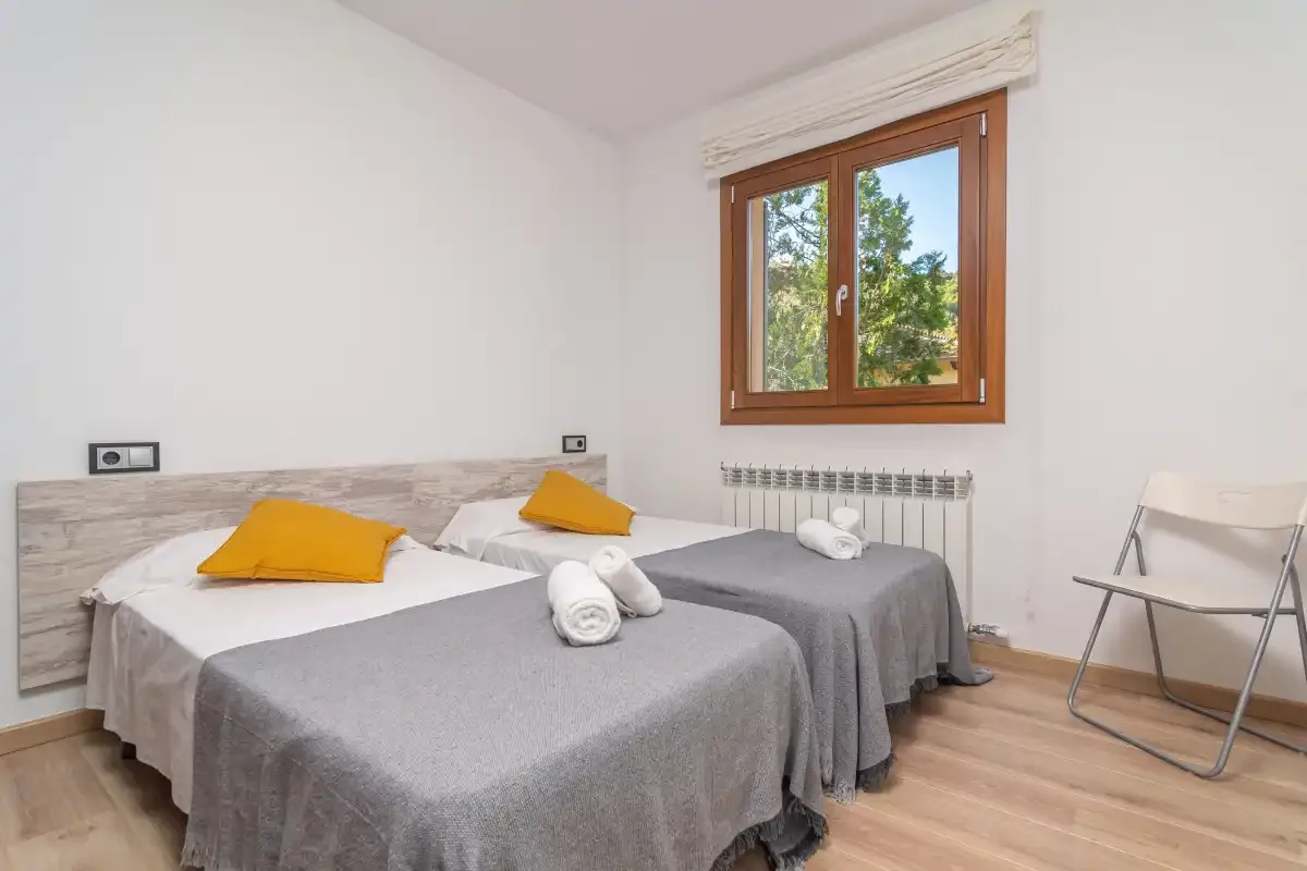 A bedroom with two beds, gray bedding, and a window overlooking trees.