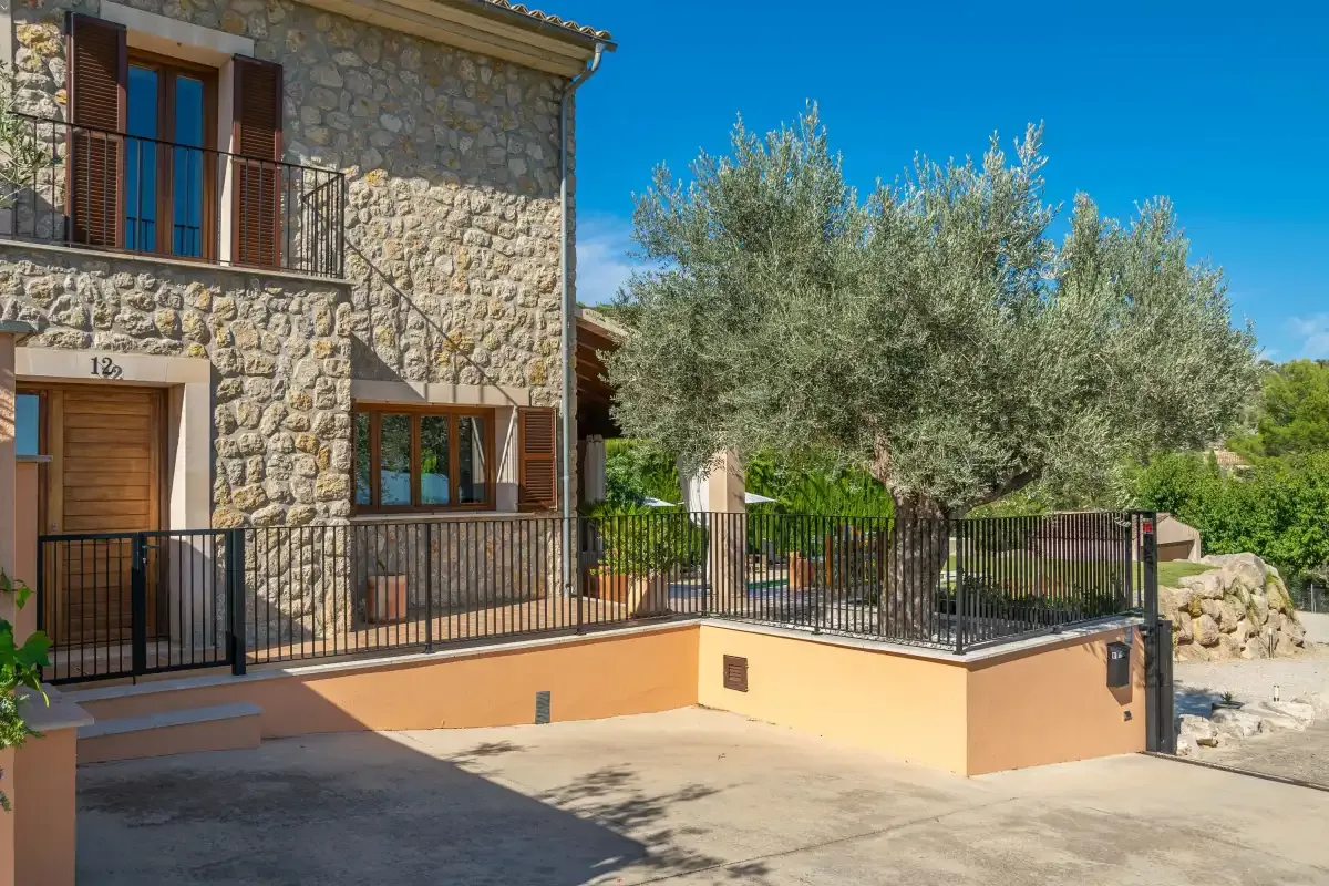 A stone house opens onto a paved terrace with black metal railings.