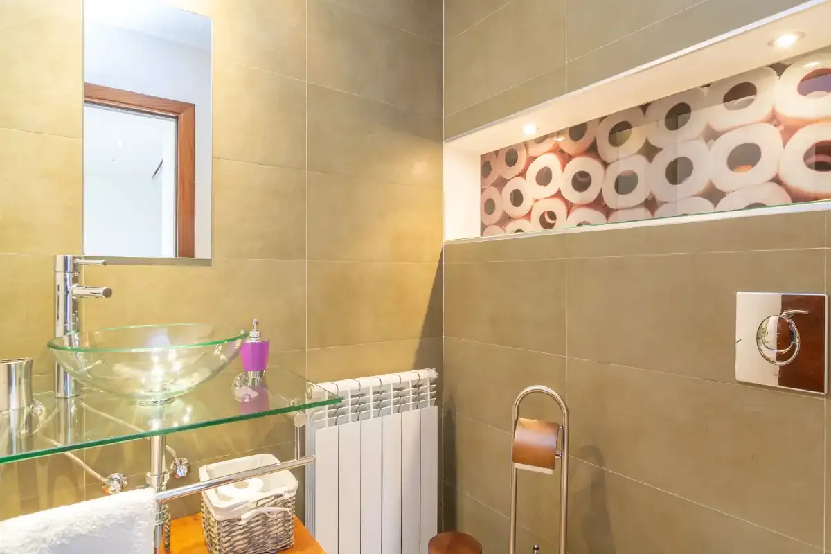 A tiled bathroom with a glass vessel sink and decorative wall lighting.