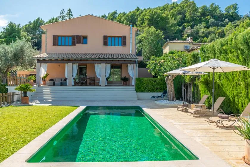 A house and swimming pool sit beside a sunny lawn and patio.