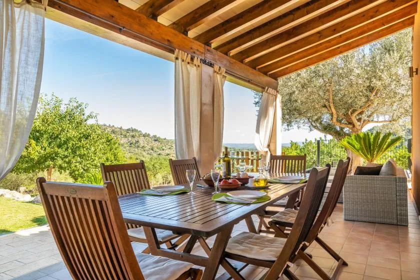 A covered outdoor dining area with a wooden table and surrounding chairs.